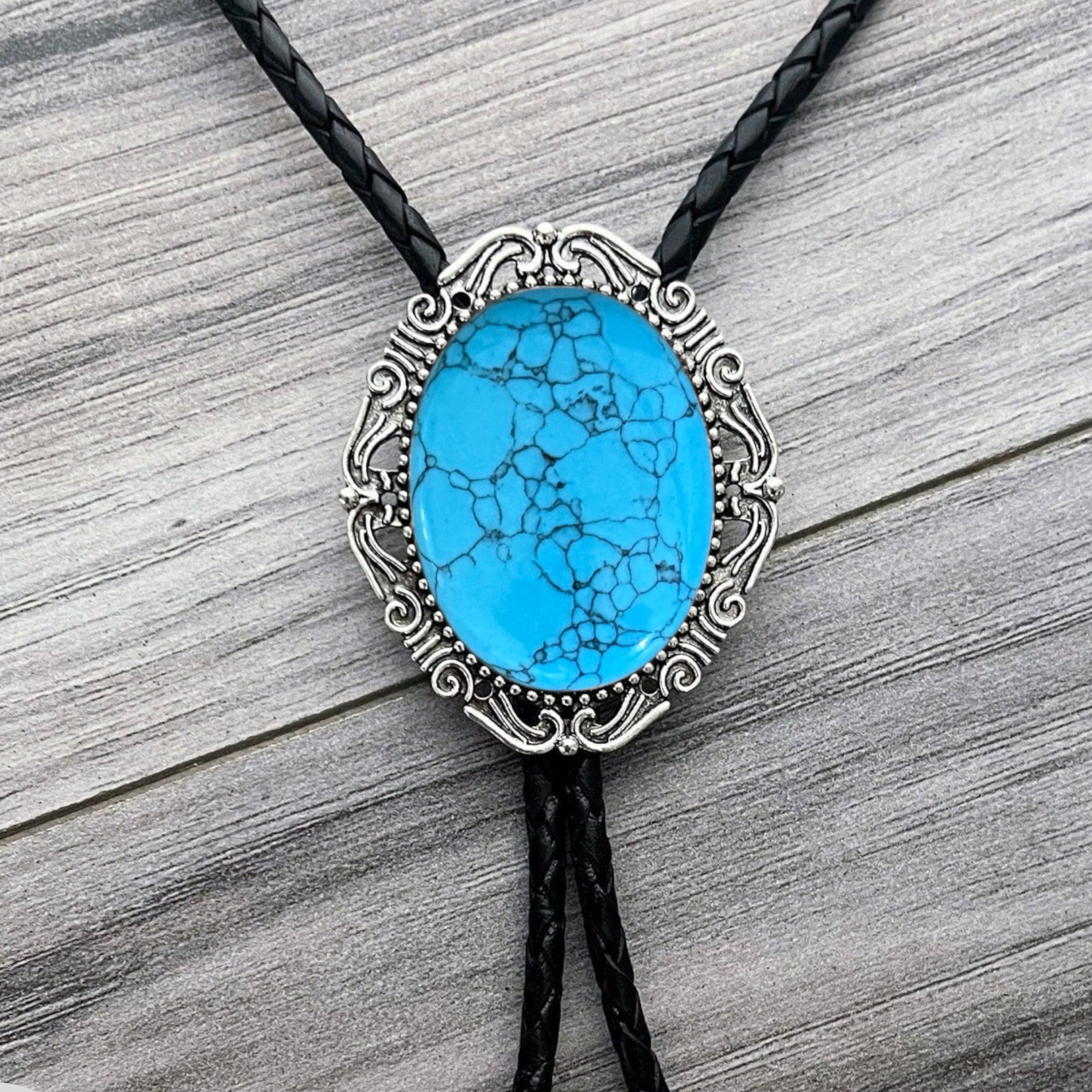 Turquoise stone bolo tie on a black braided leather cord against a wooden background