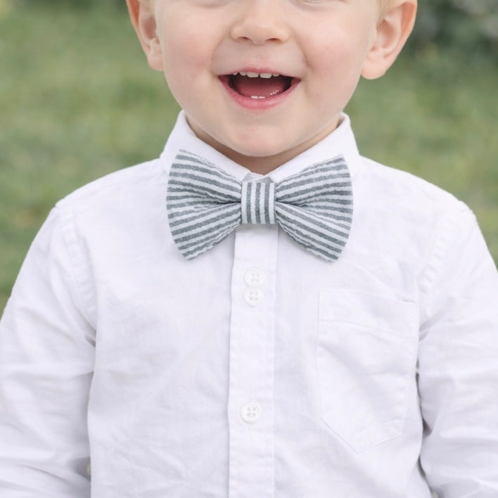 Toddler wearing a gray striped bow tie for Easter with a blurred green background