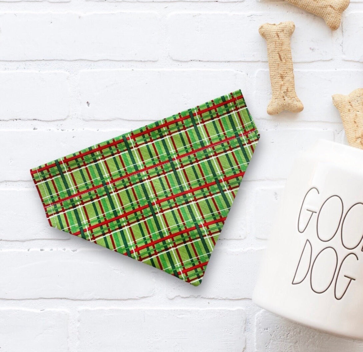 Green Christmas plaid dog bandana on a white surface with 'Good Dog' mug and dog bones.