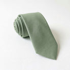 Sage tie for men rolled up on a white background.