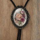 A decorative pendant featuring a floral design, including a rose and various other flowers, is displayed on a wooden surface.