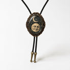 A decorative pendant featuring a moon and crescent symbol, with a smiling face, is displayed on a black cord.