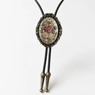 A decorative pendant featuring a floral design, hanging from a black cord with two gold-colored ends.