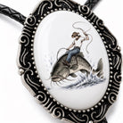 A decorative pendant featuring a cowboy riding a fish, with a detailed metal frame surrounding the image.