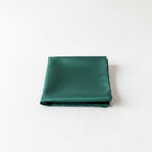 A dark green satin handkerchief is neatly folded and placed on a white surface.
