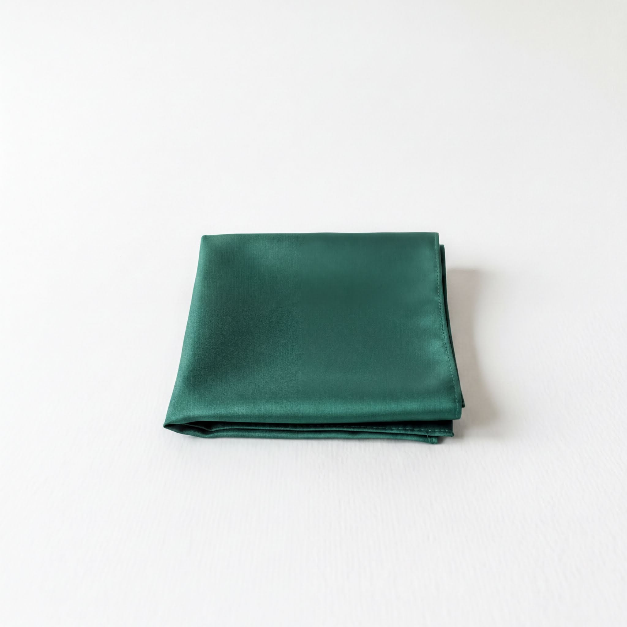 A dark green satin handkerchief is neatly folded and placed on a white surface.