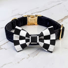 Black velvet dog collar with black and white checkered pt bowtie a gold clasp on a marble surface.