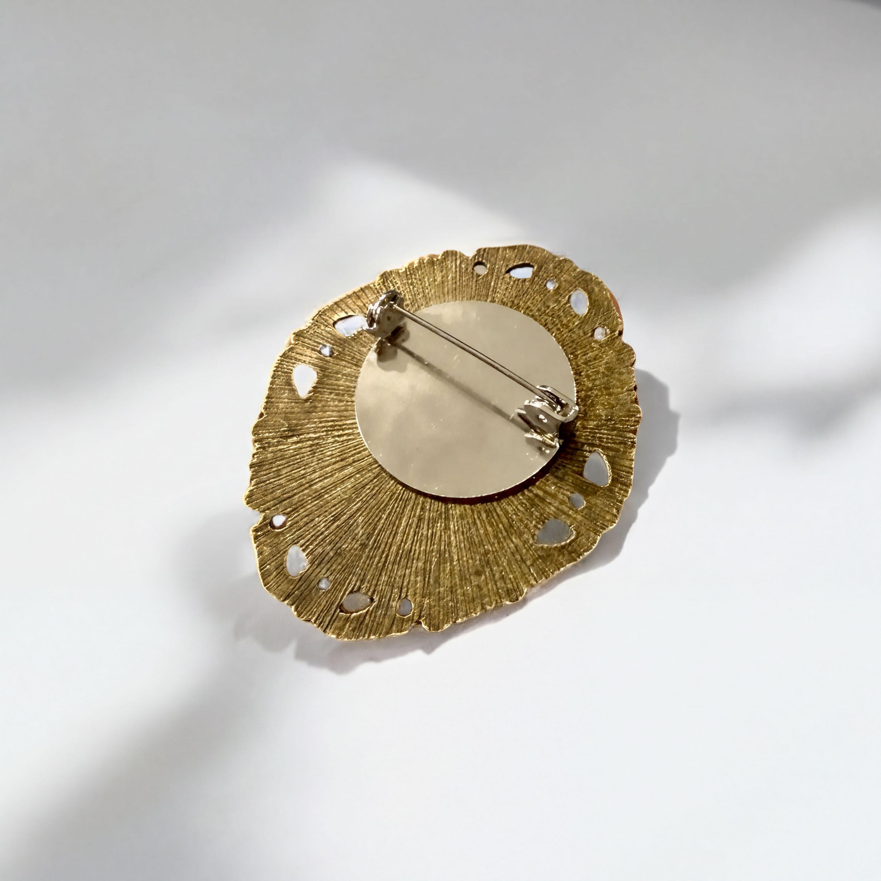 A decorative pin with a gold leaf-like design and a round center, placed on a white surface.