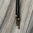 a close-up view of a black leather tie with brass-colored metal ends, resting on a wooden surface.