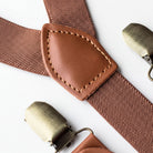 A close-up view of a brown leather suspender with a metal buckle, showing the buckle and the strap.