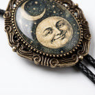 A decorative pendant featuring a moon and crescent symbol, with a smiling face in the center, is displayed on a black braided cord.