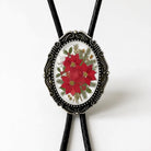 A decorative mens bolo tie featuring a floral design with red poinsettia flowers and greenery.