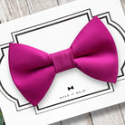 Hot pink dog bow tie on a white card with text on a wooden surface