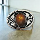 A decorative metal belt buckle with a cross design and a golden glow at the center.