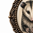 a close-up of a detailed illustration of an opossum, with its distinctive features such as its large eyes, long whiskers, and small body clearly visible. The opossum is encased within an ornate, decorative frame, which adds an elegant touch to the overall presentation.