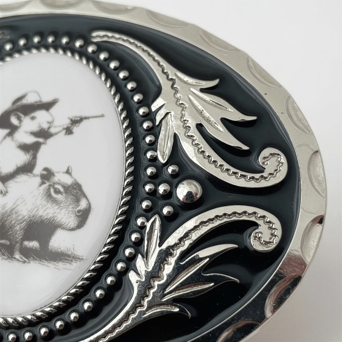 A close-up view of a decorative metal buckle featuring an engraved design with a mouse and a cowboy on a horse.