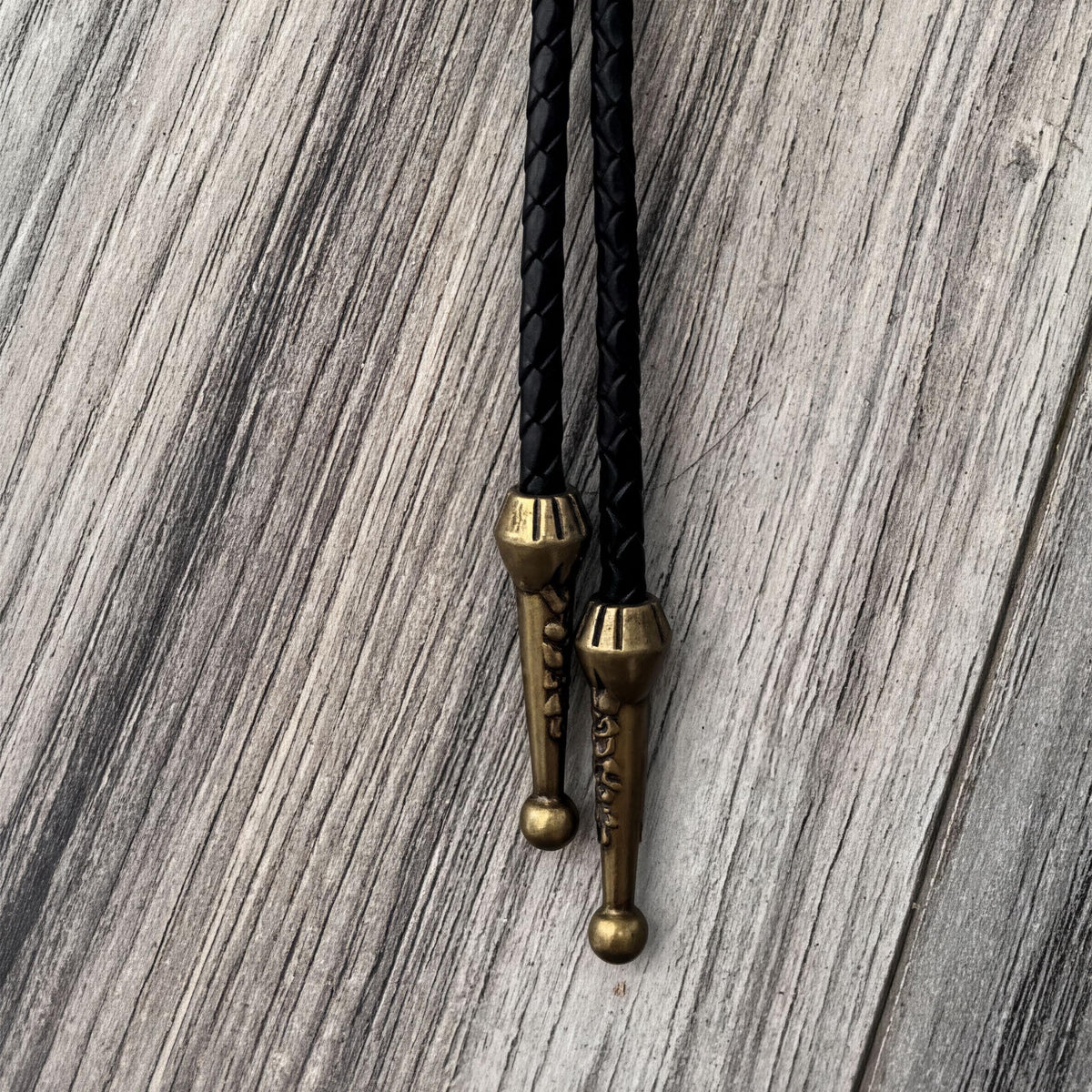 a close-up view of a black leather tie with brass-colored metal ends, resting on a wooden surface.