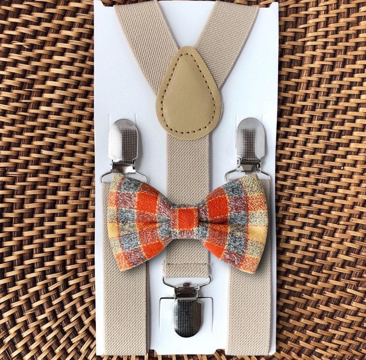 A set of fall-colored flannel bow ties and tan suspenders, displayed on a cardboard backing, with fasteners attached to the top of the bow ties.