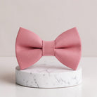 The Bold Bow Tie dusty rose pre-tied bow tie in textured matte fabric displayed on a white marble pedestal