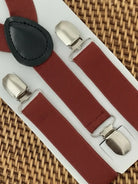 Burnt orange suspenders with silver clips on a white card against a woven background