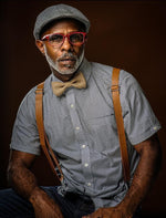 Load image into Gallery viewer, A handsome man in red glasses and a page boy hat wears a country chic burlap bow tie and rustic tan suspenders for men and boys to wear to a cowboy wedding.
